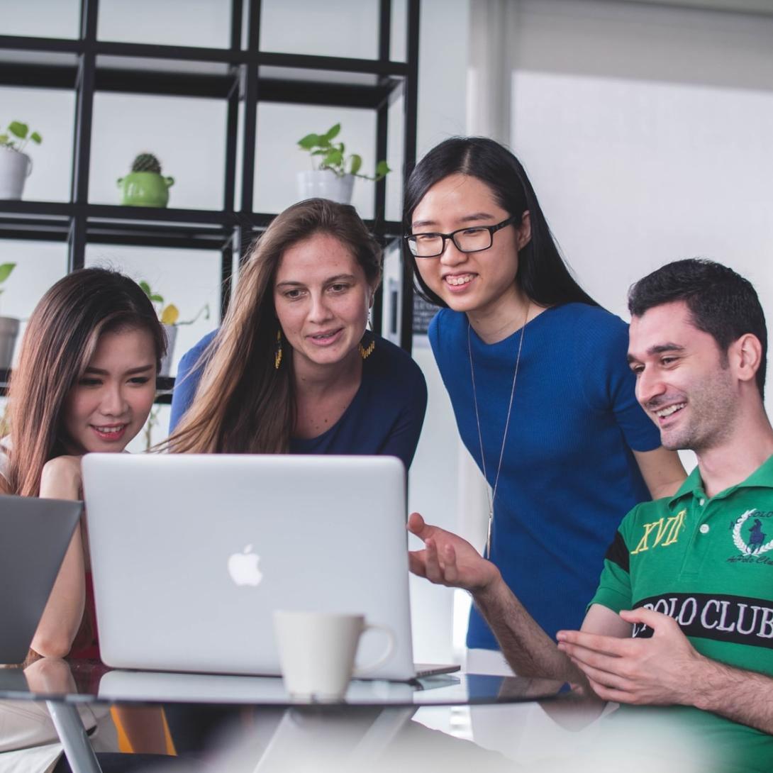 Picture of four students looking down at computer screen.